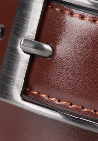 Brązowy skórzany pasek z metalową klamrą w kolorze srebrnym o wypolerowanej powierzchni, przeszyty kontrastującą jasnobrązową nicią.