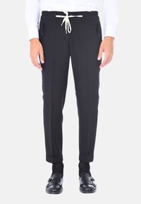 Pantaloni neri con una vestibilità affusolata, cintura elastica e cordoncino. Presentano tasche laterali e orli arrotolati. Indossati con scarpe nere.