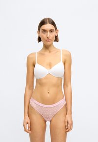 Hvit formet cup-bh med tynne stropper, kombinert med rosa gjennomsiktig stringtruse med stjernemønster. Glatte teksturer, enkelt design.