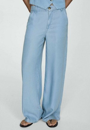 Jasnoniebieskie jeansy z wysokim stanem i szerokimi nogawkami, noszone z czarnymi sandałami typu thong, ukazujące część dopasowanego bezrękawnika.