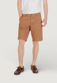 Shorts en coton marron avec une coupe classique, dotés de poches avant, de fermeture à bouton et d'une texture lisse. Associés à des chaussures en cuir marron foncé.