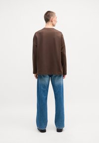 Chemise marron à manches longues avec un col rond, associée à un jean à jambes larges bleu clair. La tenue a une coupe décontractée et une texture de tissu lisse.