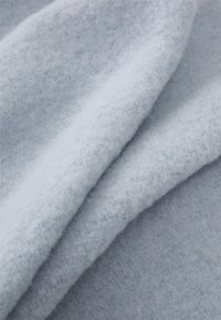 Tissu en laine bleu clair avec une finition douce et texturée, présentant des couches superposées qui créent une apparence lisse et confortable.