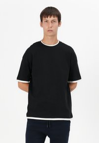 Schwarzes T-Shirt mit kurzen Ärmeln und weißen Akzenten am Rundhalsausschnitt und an den Bündchen. Aus Baumwolle gefertigt, mit einer lockeren Passform und glatter Textur.