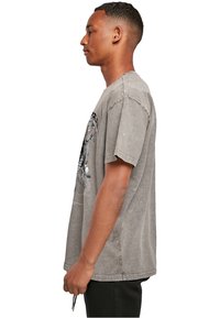 Grå oversized t-shirt lavet af bomuld med rund hals, sænket skuldre og grafisk tryk på forsiden. Sidevisning viser en afslappet pasform.
