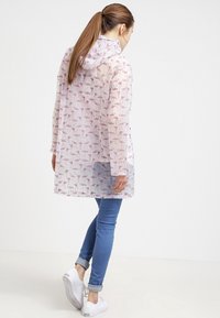 Transparent regnjacka med ett mönster av rosa flamingos, huva och långa ärmar. Bärs över blå jeans och vita sneakers.