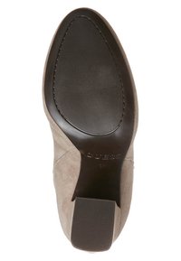 Suela de zapato de ante color beige claro con una superficie inferior negra y lisa. Presenta un tacón texturizado y un detalle de logotipo grabado.