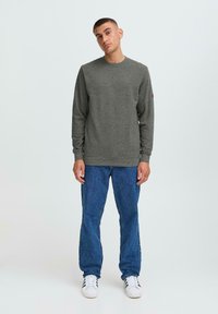Grå bomullssweatshirt med lange ermer, rund hals og ribbestrikkede mansjetter. Kombinert med blå denimjeans og hvite joggesko.
