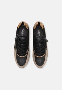 Paire de baskets noires et beiges avec des accents à imprimé léopard, détail talon doré, fermeture à lacets et fermeture éclair latérale, vue de dessus.