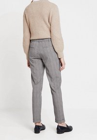 Beige stickad tröja med texturerat mönster, grå rutiga byxor och svarta skor. Byxorna har en avsmalnande passform och elastisk midja.