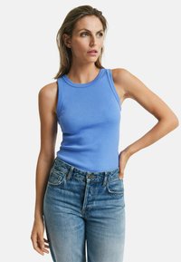 Ärmelloses blaues, geripptes Tanktop mit Rundhalsausschnitt, kombiniert mit hoch taillierten, ausgebleichten Jeans, die einen klassischen Schnitt zeigen.