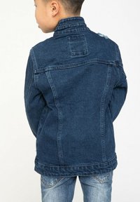 Veste en denim bleu foncé avec un col, couture de dos, et un léger effet usé sur les épaules. Texture lisse et coupe classique.