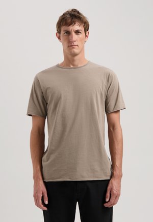 Beige Baumwoll-T-Shirt mit kurzen Ärmeln, rundem Ausschnitt und lockerem Schnitt, auf einer Person vor einem schlichten Hintergrund präsentiert.