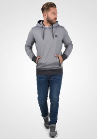Siva hoodie s vezicom, teksturirana tkanina, dva prednja džepa i crni akcenti na manžetama i pojasu, uparen sa plavim trapericama.