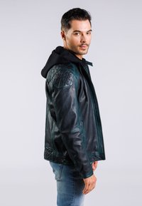 Černá kožená bunda má prošívané ramenní detaily a odnímatelnou černou kapuci, s přiléhavým střihem a hladkou texturou.