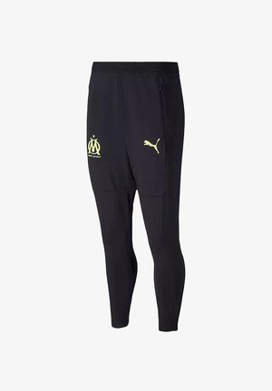 Pantalones deportivos negros hechos de un material ligero, con un diseño ajustado, logotipos amarillos de Marsella y Puma, y con bolsillos laterales con cremallera.