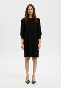 Must nagu kleit ümmarguse kaelusega, lühikeste puhvvarrukatega ja laia lõikega. Kanda terava nina ja mustade kontsadega. Sile kangastekstuuri.