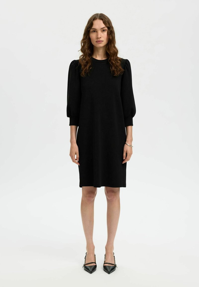 Must nagu kleit ümmarguse kaelusega, lühikeste puhvvarrukatega ja laia lõikega. Kanda terava nina ja mustade kontsadega. Sile kangastekstuuri.