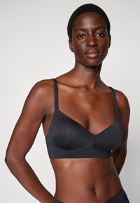Black bra with thin adjustable straps, made of smooth, stretchy material, featuring a v-neck design and seamless cups for a streamlined look.