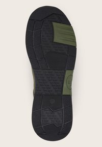 Suola in gomma nera con presa testurizzata e accenti verdi. Presenta un marchio in rilievo e indicazioni per la taglia, evidenziando un design multi-pattern.