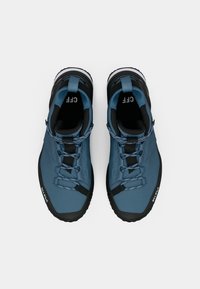 Chaussures de randonnée bleues avec une tige texturée, des accents noirs et une semelle robuste. Présente un système de laçage sécurisé et une languette au talon.