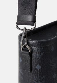 Borsa in pelle nera con texture, caratterizzata da una finitura liscia, dettagli incisi e un gancio metallico di attacco su una tracolla a fantasia.