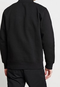 Zwarte sweatshirt met een hoge kraag, lange mouwen en ribgebreide manchetten. Gemaakt van gestructureerde stof, met een eenvoudig, minimalistisch ontwerp.