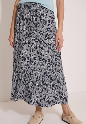 Personne portant une jupe midi à motif cachemire bleu marine et blanc, un haut bleu clair et des chaussures beige à enfiler.