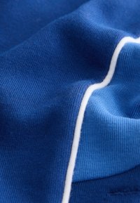 Gros plan d'un tissu bleu avec une texture tricotée visible et une bande blanche incurvée traversant le matériau en diagonale.