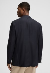 Granatowa marynarka z teksturowanej tkaniny, z klasycznym kołnierzem, dwoma guzikami na rękawach i pojedynczym rozcięciem z tyłu.