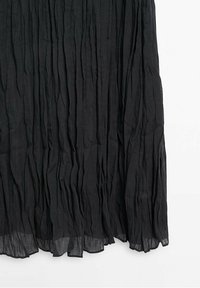 Tissu noir plissé avec des froissements verticaux et une texture légèrement transparente au bord inférieur sur un fond blanc.