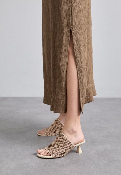 Beige opentå mules med et teksturert mesh-overdel og en lav, firkantet hæl, kombinert med en brun, ripet kjole med en sideslitt.