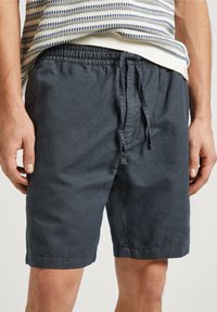 Męskie granatowe bawełniane szorty z elastycznym pasem i sznurkiem, noszone z paskowanym swetrem.