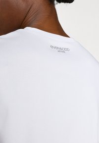 Weißes Sport-T-Shirt mit strukturiertem Stoff. Verfügt über einen rundhalsausschnitt und den Markennamen "even&odd ACTIVE" auf der Rückseite gedruckt.