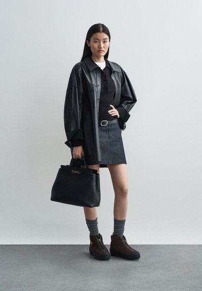 Sort læder oversized skjorte, sort polo, mørk denimnederdel, sort håndtaske, brune støvler med grå sokker. Enkel, moderne og struktureret design.