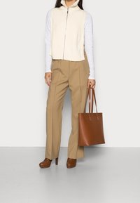 Béžový žebrovaný svetr na zip, bílá košile s dlouhým rukávem, hnědé kalhoty na míru, hnědá kožená taška a hnědé lodičky.