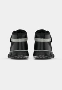 Et par svarte høye sneakers med grå reflekterende stropper og stjerne mønster på sålen, sett fra baksiden på en hvit bakgrunn.
