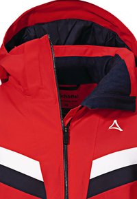 Rote wasserdichte Jacke mit Reißverschluss vorne, versehen mit weißen und navyblauen Streifen. Kapuze mit weichem Innenfutter und einem Logo auf der Brust.