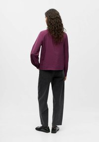 Lila leichtgewichtige Bluse mit strukturierter Oberfläche, kombiniert mit hoch taillierten dunkelgrauen Jeans und schwarzen Schuhen, von hinten betrachtet.