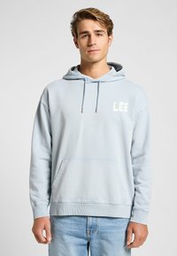 Felpa con cappuccio azzurro chiaro realizzata in materiale morbido. Presenta una tasca frontale e un logo "LEE" bianco sul petto. Vestibilità standard con polsini a coste.