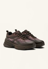 Brown and purple mesh athletic shoes with textured panels, padded collar, and thick rubber sole, featuring contrasting laces and branding detail.