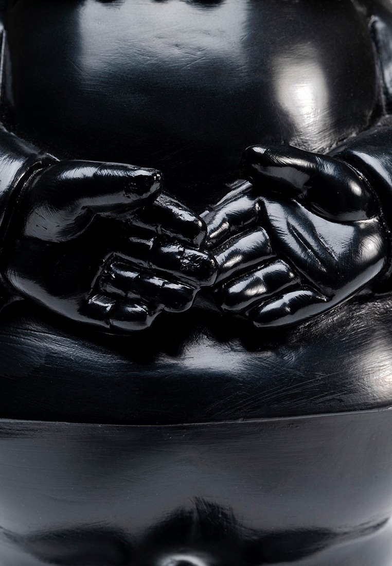 Mains en céramique noire brillante reposant ensemble sur un ventre arrondi, suggérant une statue de Bouddha assis.