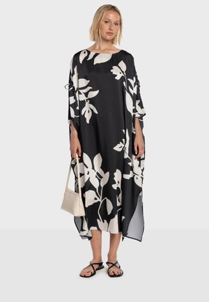 Czarno-biała kwiatowa kaftan o luźnym kroju, szerokich rękawach i dekolcie w kształcie łódki. Tkanina jest lekka i zwiewna, zestawiona z sandałami na ramiączkach.