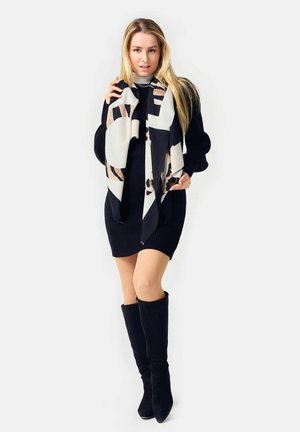 Knit black dress with long sleeves, paired with a patterned scarf in cream, black, and brown. Model wears knee-high black boots.