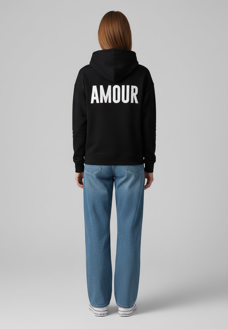 Felpa nera con cappuccio con la scritta "AMOUR" stampata in bianco sul retro, abbinata a jeans a gamba larga blu chiaro e sneakers bianche.
