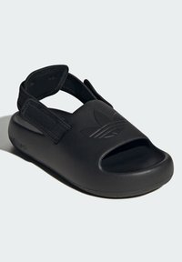 Black sandal with open toe and adjustable strap. Made from textured material, featuring a raised logo on the upper and a solid sole.