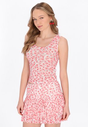 Fiatal nő rózsaszín cseresznyés mintás ujjatlan felsőt és hozzá illő fodros miniszoknyát visel, cseresznye alakú fülbevalóval.