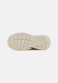 Sula av en sneaker som visar ett strukturerat gummimaterial i ljus beige med ett mönstrat suldesign för grepp och dragkraft.