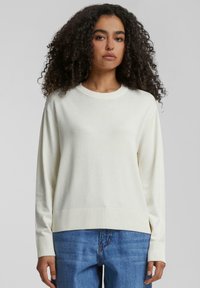 Pull léger beige à manches longues, avec des poignets et un ourlet côtelés. Design simple avec un col rond. Porté avec un jean en denim bleu. Texture douce.