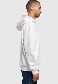 Hvit hettegenser med løs passform, kengurulomme og ribbestrikkede mansjetter. Brukes over blå jeans, med en uformell stil.
